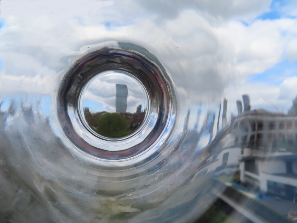 The image shows blurred and distorted city buildings through the bottom of an empty drinking glass